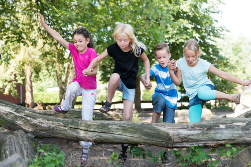 Vier Kinder springen lachend über einen Baumstamm