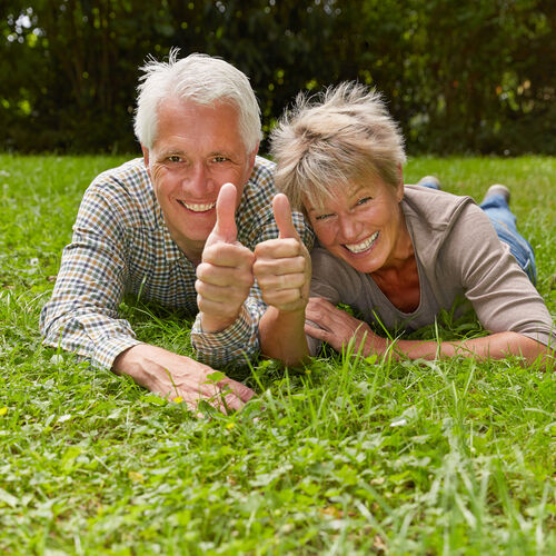 Eine Mann und eine Frau liegen auf einer Wiese und zeigen die Geste Daumen hoch.