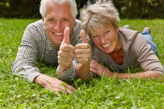 Eine Mann und eine Frau liegen auf einer Wiese und zeigen die Geste Daumen hoch.