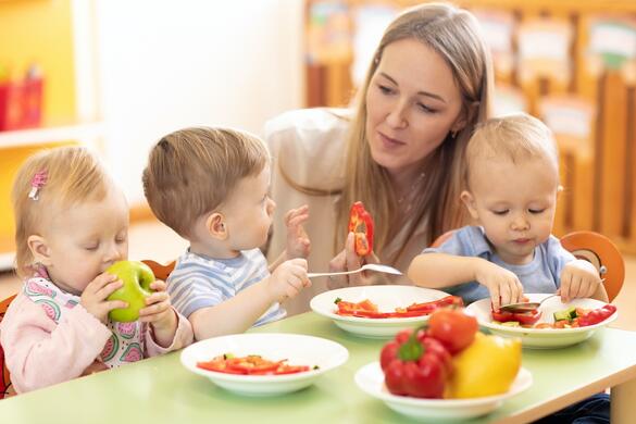 Drei Kindergartenkinder sitzen am Tisch und essen Gemüse