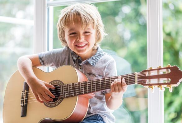 Kleiner Junge spielt fröhlich auf einer Gitarre